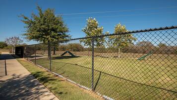 A fenced outdoor area with a grassy field, trees, and a playground.