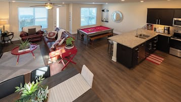 A modern living room with a pool table, a dining area, and a kitchen with a central island.