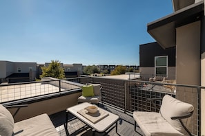 Eine Dachterrasse mit Sitzgelegenheiten im Freien, einem Tisch mit einer Schale und Blick auf benachbarte Gebäude.