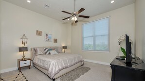 A bedroom with a bed, a ceiling fan, a nightstand with a lamp, a desk with a monitor, and a window with blinds. - "Pooling Around " in Aggieland" (College Station)