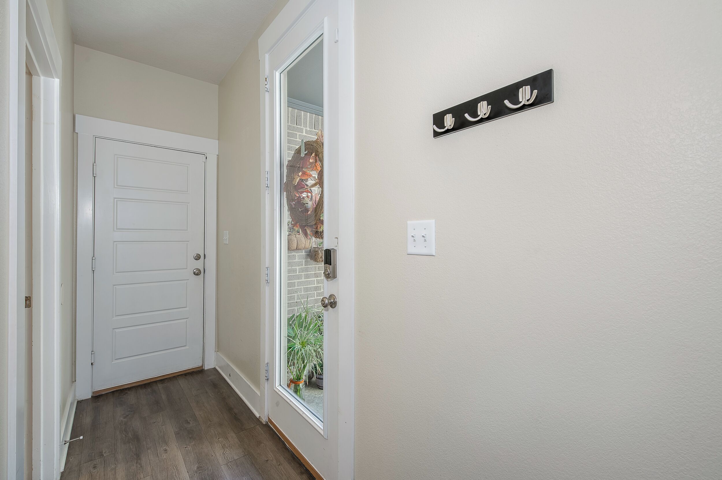 A hallway with a white door, a glass door leading outside, and a wall-mounted sign with Arabic script.