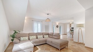 Ein modernes Wohnzimmer mit einer Eckcouch, einer Stehlampe und einem Essbereich im Hintergrund.