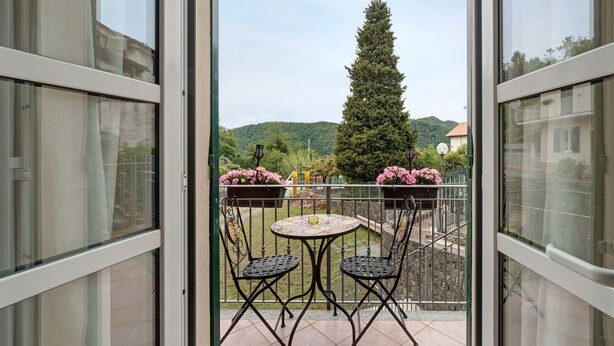 Ein Balkon mit zwei Stühlen und einem Tisch, Blick auf einen Baum und ein fernes Gebirge.