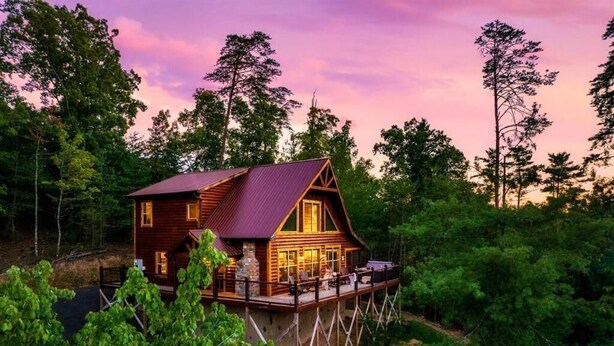 Une cabane en bois dotée d’un balcon, entourée d’arbres et construite sur pilotis.