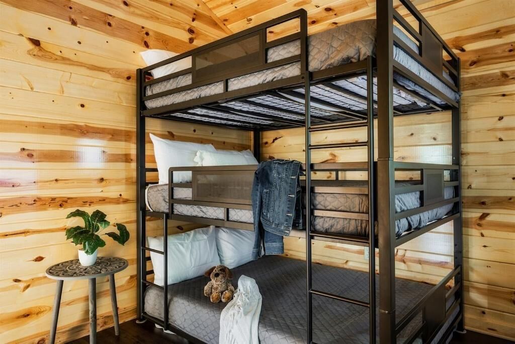 Une chambre avec un lit superposé aux murs en bois, une petite table ronde avec une plante et un ours en peluche sur le lit du bas.