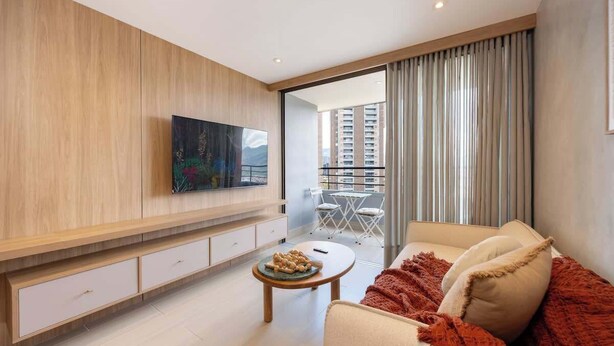 A modern living room with a sofa, a coffee table, a TV mounted on the wall, and a balcony with a view of high-rise buildings. - lEPl Luxury&Elegant Apt W/ Ac & Pool Near Provenza (Medellín)