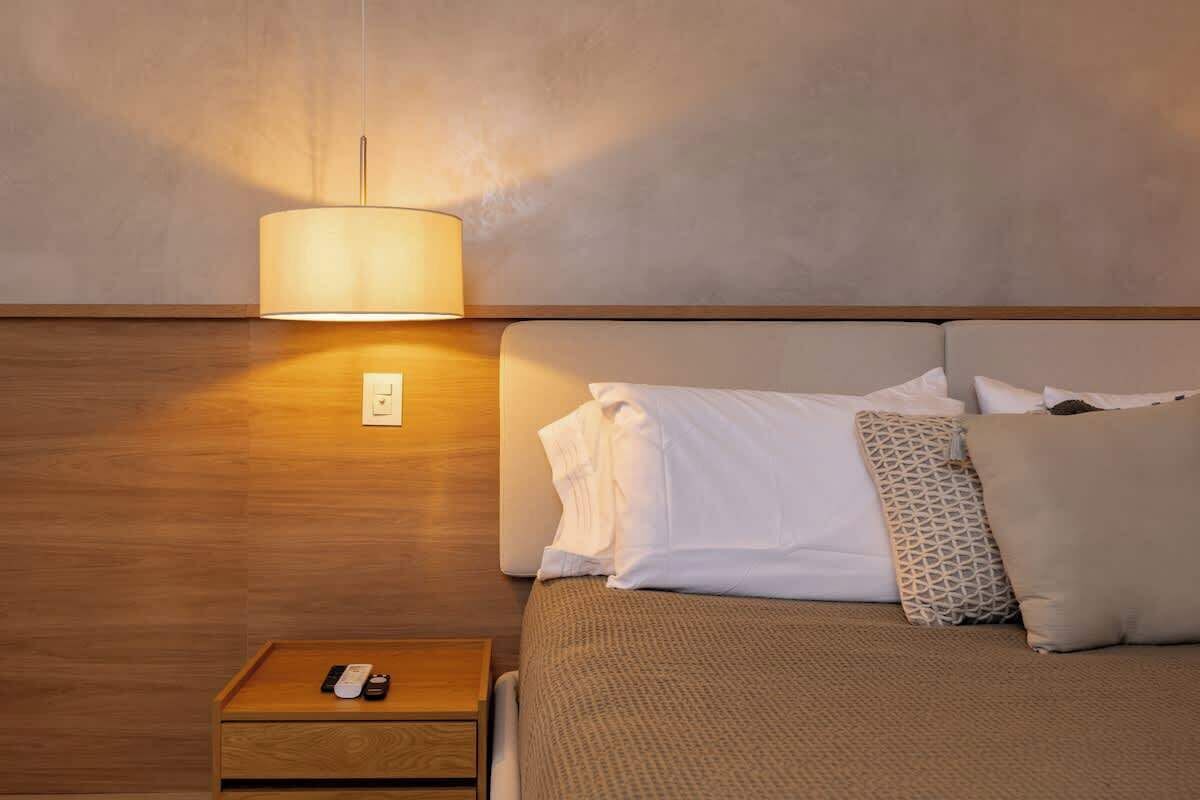 Una habitación de hotel con una cama, una mesita de noche con control remoto y una lámpara de pared.
