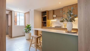 A modern kitchen with a bar area, wooden cabinets, and a large potted plant. - lEPl Luxury&Elegant Apt W/ Ac & Pool Near Provenza (Medellín)