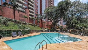 Una piscina con sillas de descanso, un puesto de socorrista y un edificio de ladrillo rojo al fondo.