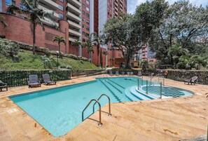 A swimming pool with lounge chairs, a lifeguard stand, and a red brick building in the background. - lEPl Luxury&Elegant Apt W/ Ac & Pool Near Provenza (Medellín)