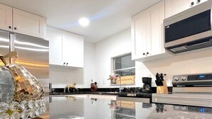Une cuisine moderne dotée d’un plan de travail en marbre, d’appareils électroménagers en acier inoxydable et de meubles blancs.