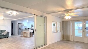 Un vaste espace de vie doté d’une porte-fenêtre coulissante donnant sur la cuisine, d’un ventilateur de plafond et d’un luminaire.