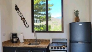 Une cuisine de taille réduite, équipée d’une cuisinière, d’un réfrigérateur et d’une fenêtre donnant sur les arbres.