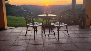 Une terrasse extérieure avec une table et des chaises, offrant une vue sur un paysage magnifique et un coucher de soleil.