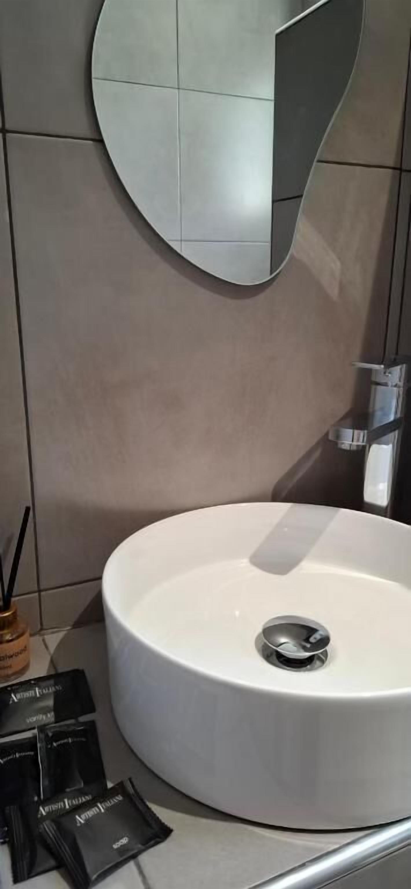 Une salle de bain avec un lavabo rond blanc, un miroir et un porte-serviettes.