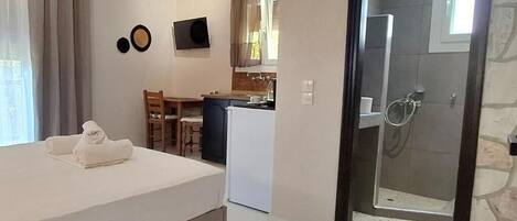 Ein Schlafzimmer mit Bett, einer kleinen Küchenzeile, einer Dusche und einem Essbereich.