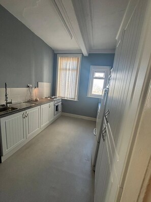 A narrow kitchen with white cabinets, a stove, and a window with blinds. - Room-serene Ocean-view Apartment Room in (Sunderland)