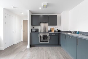 A modern kitchen with grey cabinets, a stainless steel refrigerator, a built-in oven, and a countertop with a sink. - George House by Guestz (Wakefield)