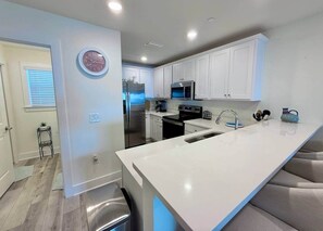 A modern kitchen with white cabinetry, stainless steel appliances, and a large island with a sink. - Blue Heron: Kayaks, Bay Views & more! (Escambia County)