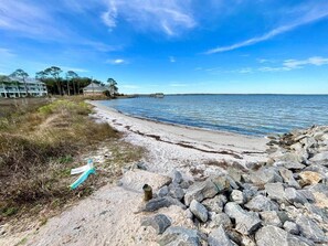 A beach with a rocky shoreline, a clear sky, and a distant pier. - Blue Heron: Kayaks, Bay Views & more! (Escambia County)