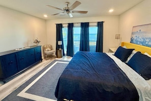 A bedroom with a bed, a ceiling fan, a nightstand, a chair, and a view of the outdoors. - Bay View 108: Great Views, Pool & More! (Escambia County)