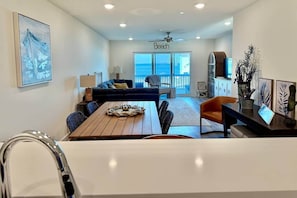 A modern living room with a dining area, a sofa, a coffee table, and a view of the beach. - Bay View 108: Great Views, Pool & More! (Escambia County)