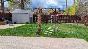 Un jardin avec une clôture en bois, un abri de jardin, une pergola et un chemin pavé.