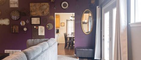 Una sala de estar con un sofá gris, un comedor con mesa y sillas, y un pasillo que conduce a una puerta.