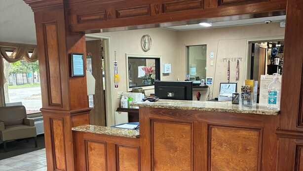 A reception area with a wooden counter, a clock, a computer, and a caution sign. - Hometown inn (Flint)