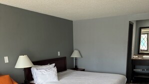 A hotel room with a bed, two bedside lamps, a chair, and a desk. - Hometown inn (Flint)