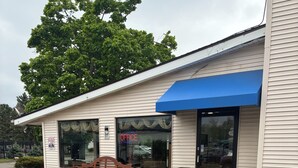 A building with a blue awning, a bench, and potted plants in front. - Hometown inn (Flint)