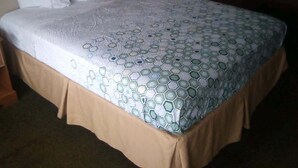 A bed with a patterned bedspread, a brown skirted bed base, and white pillows. - Hometown inn (Flint)