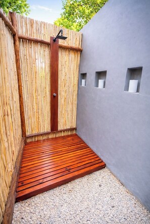 Eine Holztür führt zu einem überdachten Außenbereich mit einer Holzterrasse und einer grauen Wand mit kleinen Fenstern.