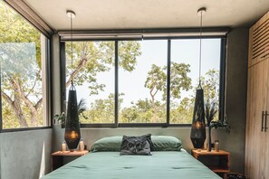 Ein Schlafzimmer mit großem Fenster, einem Bett mit grüner Bettwäsche, zwei Nachttischen mit Lampen und Blick auf Bäume.