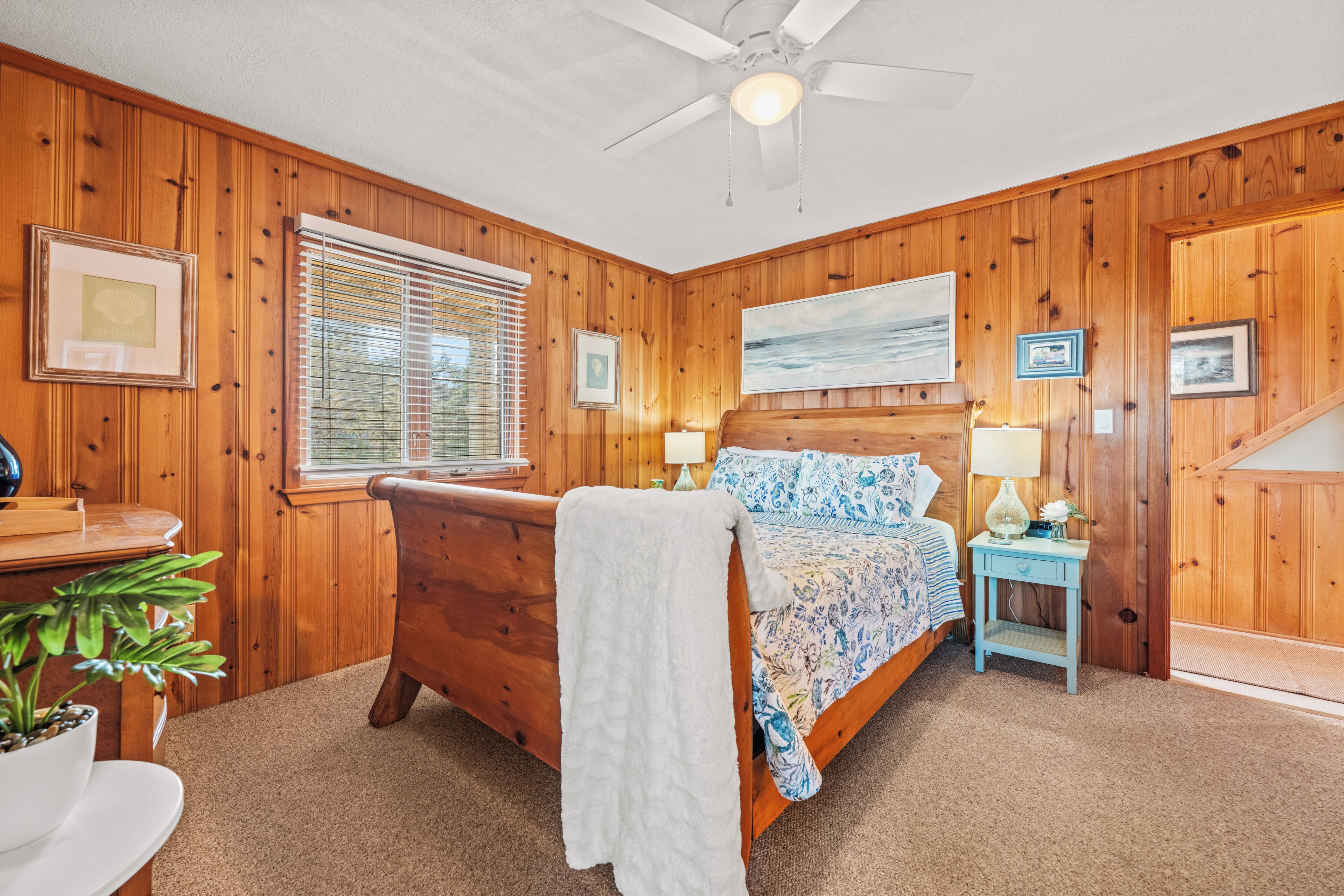 A wooden-paneled bedroom with a bed, bedside tables, a ceiling fan, and a window with blinds.
