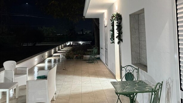 Eine moderne Terrasse im Freien mit weißen Korbmöbeln, einem grünen Metalltisch und Blick aufs Wasser.