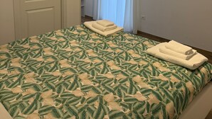 Ein Schlafzimmer mit Bett, Fernseher, Tür und einem Fenster mit Vorhängen.