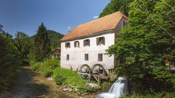Ein rustikales Gebäude mit einer Stein-Fassade, einem roten Ziegeldach und einem Wasserrad.
