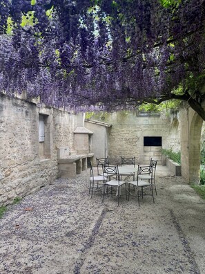 A stone-walled courtyard with a table and chairs, surrounded by a pergola with purple flowers. - Spacious house in Provence Swimming pool 10 people (Beaucaire)