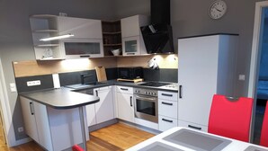 A modern kitchen with white cabinets, a black stove, and a red chair.