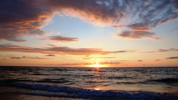 A sunset over the ocean with clouds in the sky.