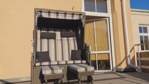 A sunlit outdoor seating area with a striped sofa and two chairs, a small table, and a window with a view of the sky.