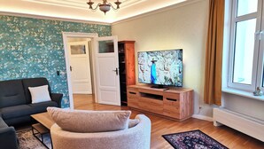 A living room with a black sofa, a grey bean bag, a wooden TV stand, and a large painting on the wall.