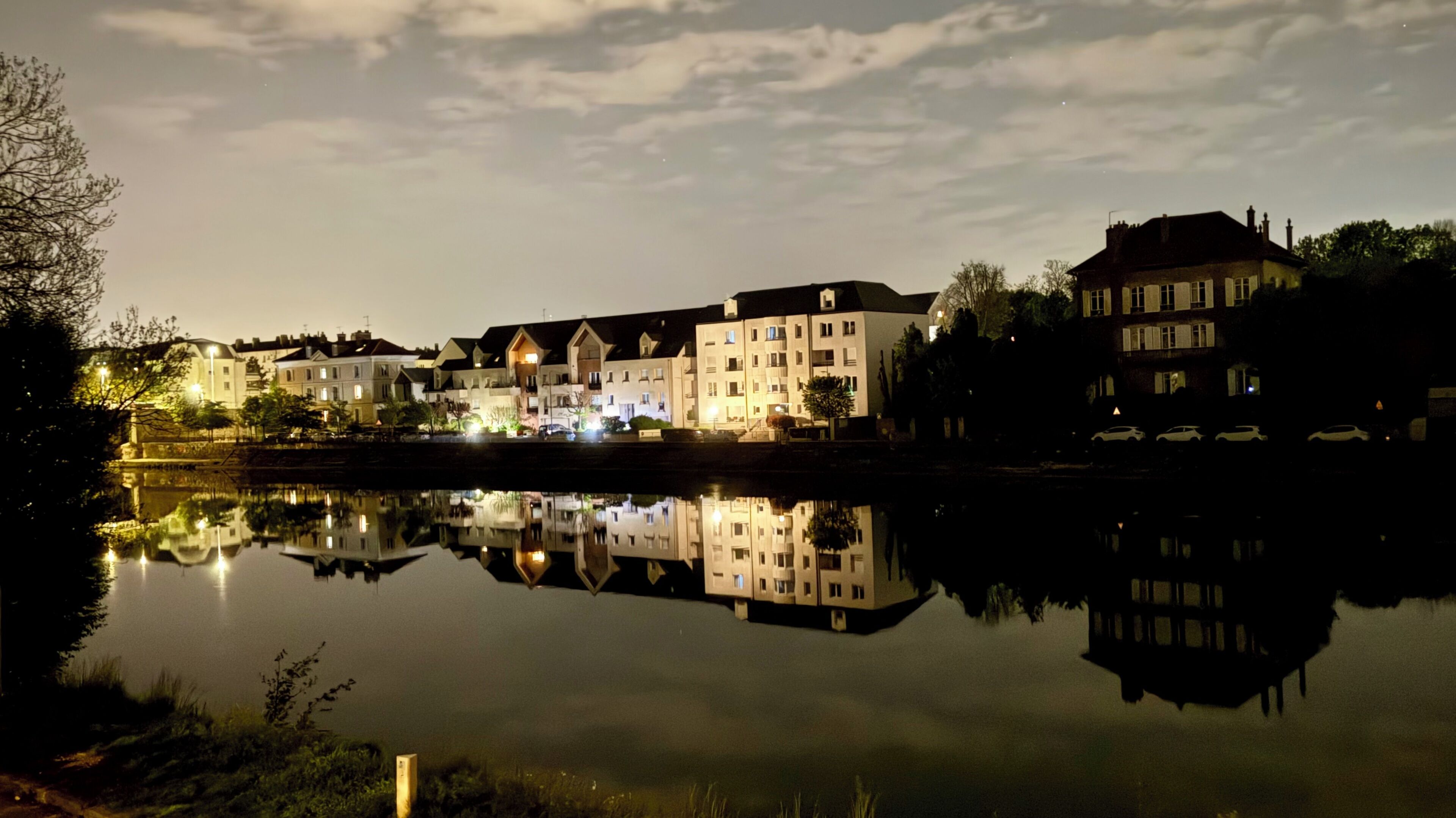 Ein ruhiger Fluss spiegelt Gebäude mit mehreren Stockwerken, eine Brücke und einen klaren Himmel wider.