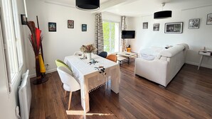 Una sala de estar moderna con comedor, muebles blancos y un televisor de pantalla plana.