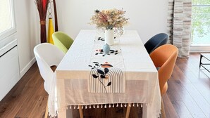 Un comedor con una mesa lista para cuatro personas, una lámpara colgante y carteles enmarcados en la pared.