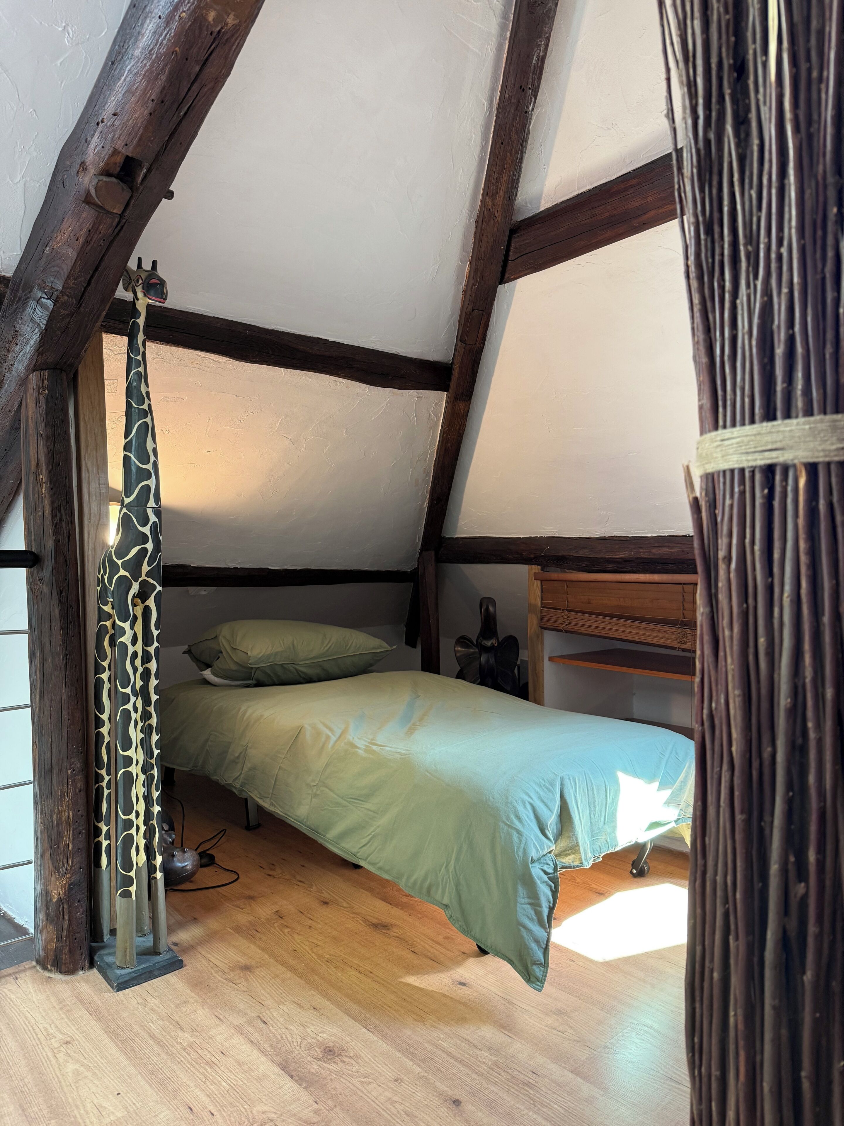 Een knus zolderkamertje met een enkel bed, een houten plafond en een gordijn in de vorm van een giraffe.