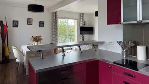 Una cocina moderna con una isla central, un comedor con mesa blanca y vistas a la vegetación.
