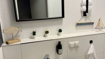 Un bany amb un rentamans blanc, un mirall, un suport per a tovalloles, un dispensador de sabó i una petita planta en test.