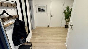En gang med et knagered, et indrammet billede, en dør og en potteplante.